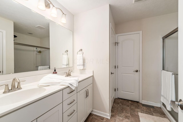 full bathroom with baseboards, a shower with shower door, double vanity, and stone finish flooring