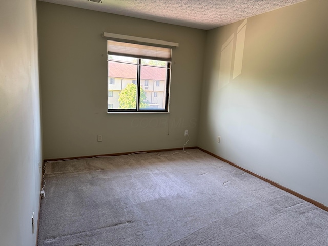 empty room featuring a textured ceiling, carpet floors, and baseboards