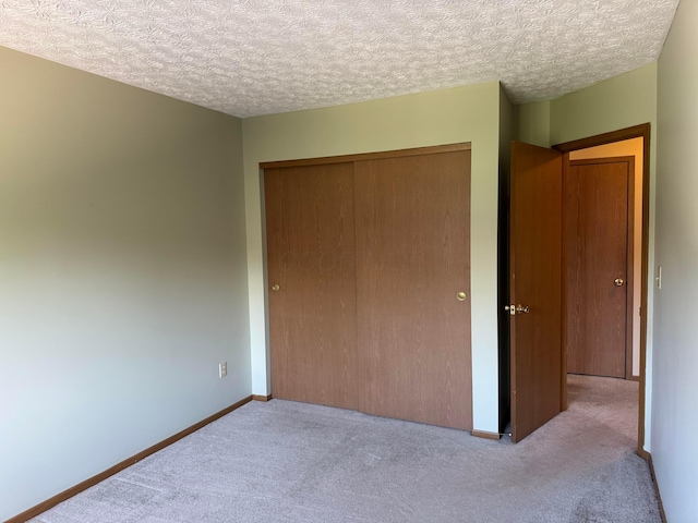 unfurnished bedroom featuring carpet, a textured ceiling, a closet, and baseboards