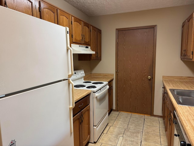 kitchen with under cabinet range hood, brown cabinetry, light tile patterned floors, white appliances, and a sink
