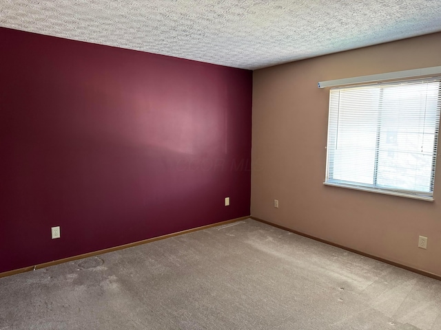 carpeted spare room featuring a textured ceiling and baseboards