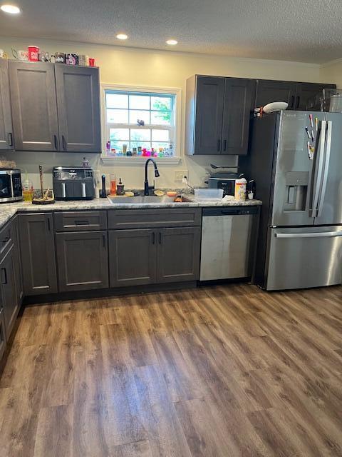 kitchen featuring a textured ceiling, a sink, wood finished floors, light countertops, and appliances with stainless steel finishes