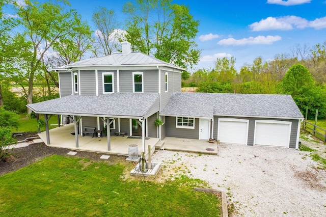 farmhouse with a front lawn, a garage, a chimney, covered porch, and gravel driveway