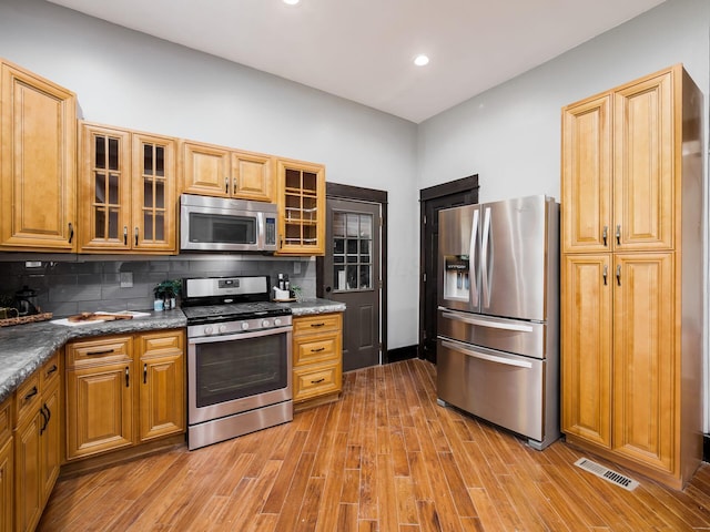 kitchen featuring stainless steel appliances, visible vents, decorative backsplash, and light wood-type flooring