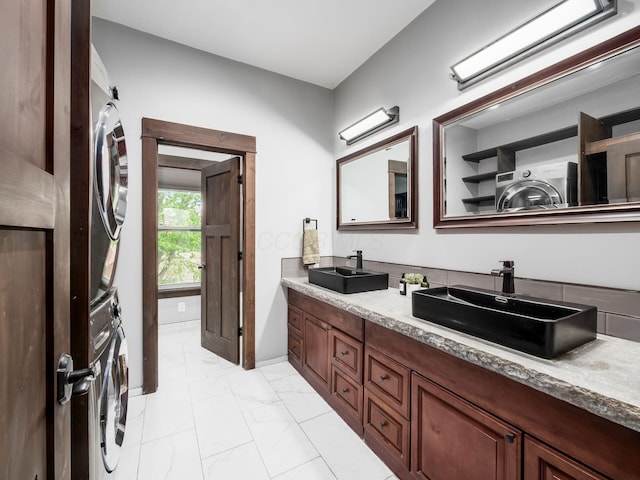 full bath featuring stacked washing maching and dryer, double vanity, a sink, and marble finish floor