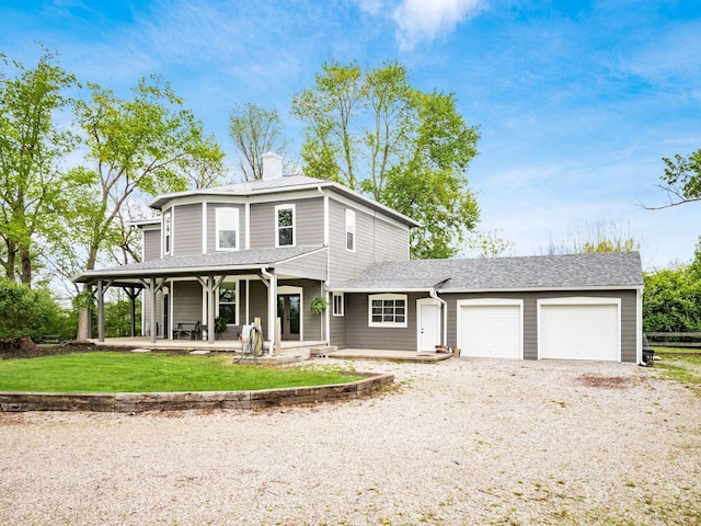 view of front of house featuring a front lawn, a garage, a chimney, covered porch, and gravel driveway