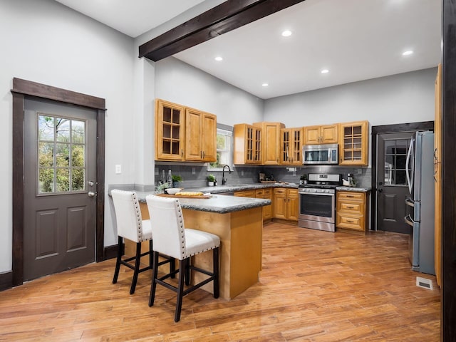kitchen with appliances with stainless steel finishes, light wood-style floors, a peninsula, a kitchen bar, and visible vents