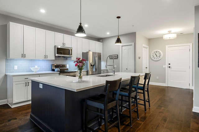 kitchen featuring a sink, a center island with sink, light countertops, decorative backsplash, and appliances with stainless steel finishes