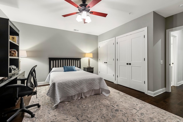 bedroom with wood finished floors, visible vents, two closets, ceiling fan, and baseboards