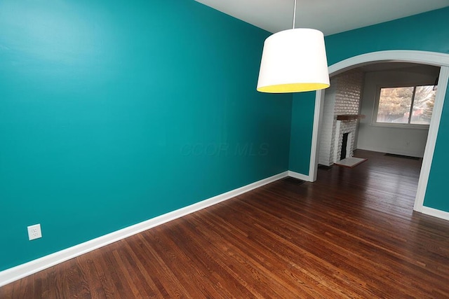 unfurnished dining area with baseboards, arched walkways, dark wood-style flooring, and a brick fireplace