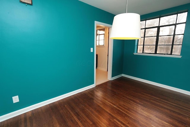 spare room featuring baseboards, plenty of natural light, and dark wood-type flooring