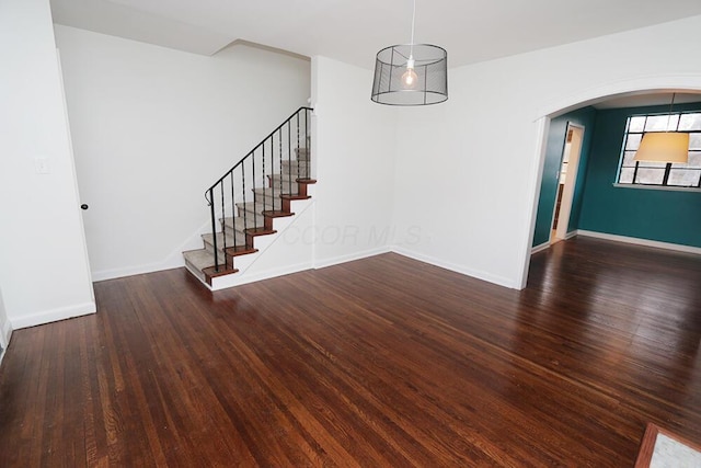 unfurnished dining area featuring arched walkways, baseboards, stairs, and wood finished floors