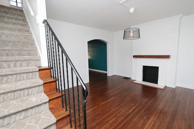 stairway featuring visible vents, wood finished floors, a fireplace, baseboards, and arched walkways