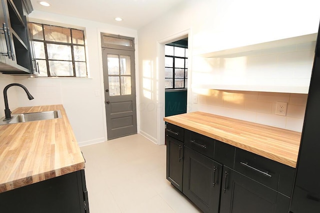 interior space featuring tasteful backsplash, a sink, dark cabinets, recessed lighting, and butcher block countertops