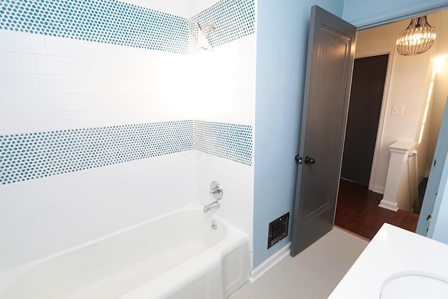 bathroom with a sink, washtub / shower combination, baseboards, and a notable chandelier