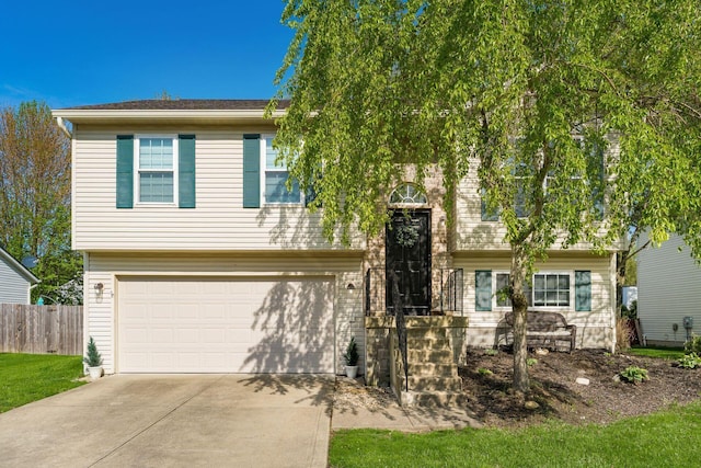 raised ranch with a garage, fence, and concrete driveway