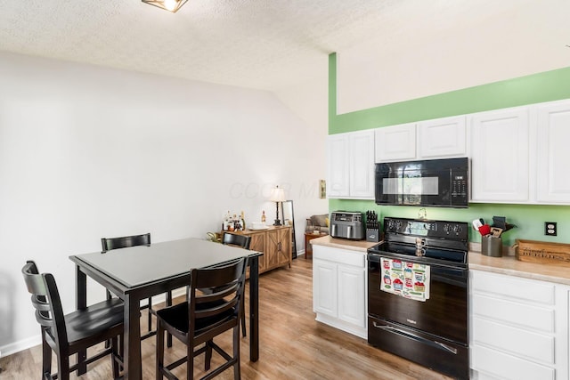 kitchen featuring light countertops, white cabinets, light wood-style flooring, black appliances, and vaulted ceiling