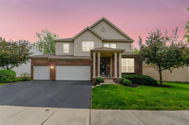 traditional home featuring brick siding, an attached garage, a front yard, and aphalt driveway