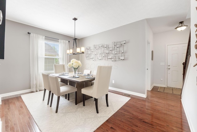 dining area with visible vents, baseboards, wood finished floors, and a notable chandelier