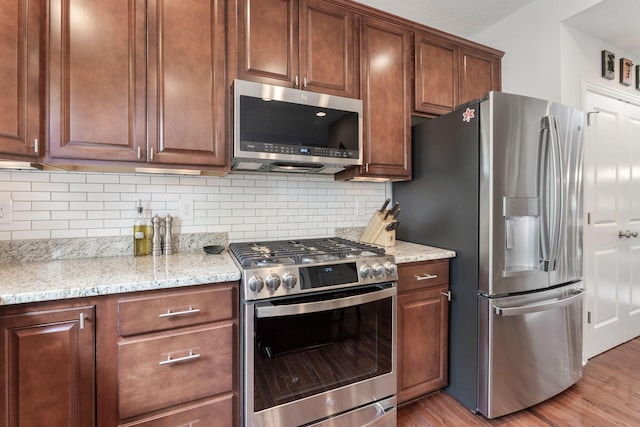 kitchen with appliances with stainless steel finishes, tasteful backsplash, light stone countertops, and light wood finished floors