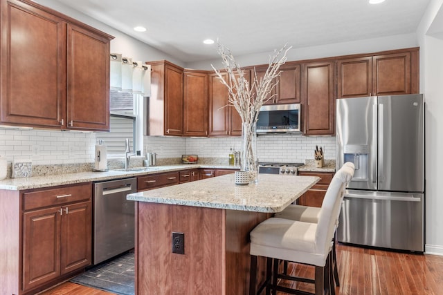 kitchen with light stone countertops, appliances with stainless steel finishes, a breakfast bar area, a kitchen island, and dark wood-style floors