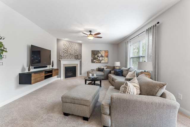 living area featuring a tiled fireplace, a ceiling fan, baseboards, and light carpet