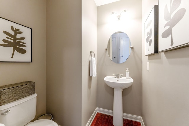 half bathroom featuring baseboards, a sink, wood finished floors, and toilet
