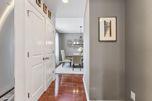 corridor with dark wood-style flooring, baseboards, and a notable chandelier
