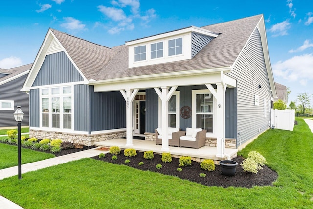 view of front of property featuring a porch, stone siding, a front lawn, board and batten siding, and a shingled roof
