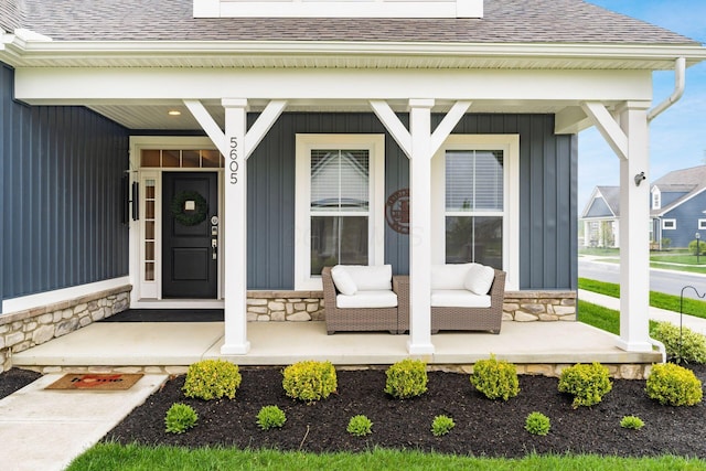 doorway to property with stone siding, a porch, roof with shingles, and board and batten siding
