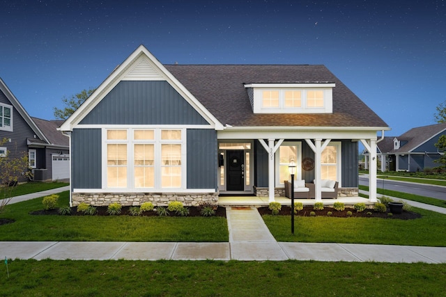 modern farmhouse style home with board and batten siding, cooling unit, covered porch, stone siding, and a front lawn