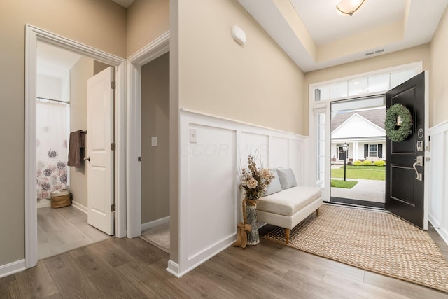 foyer entrance with a tray ceiling, a decorative wall, visible vents, and wood finished floors