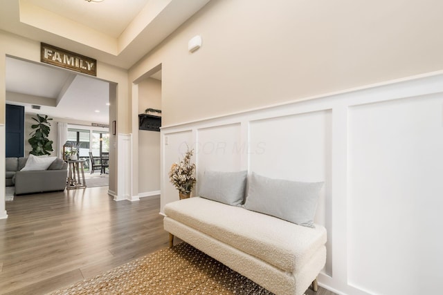 living area with a raised ceiling, a decorative wall, and wood finished floors