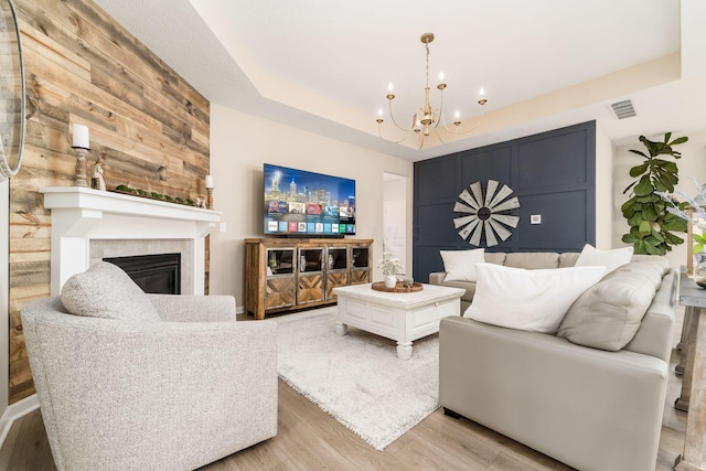 living room featuring a glass covered fireplace, visible vents, a chandelier, a raised ceiling, and light wood-type flooring