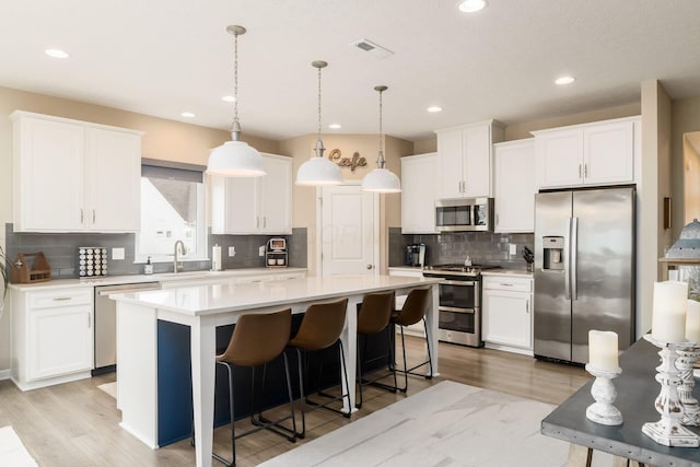 kitchen with light wood finished floors, a center island, stainless steel appliances, light countertops, and tasteful backsplash