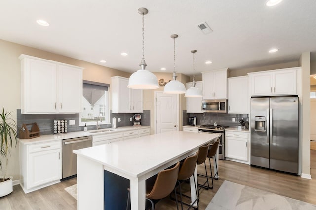 kitchen with a sink, tasteful backsplash, white cabinets, a kitchen island, and appliances with stainless steel finishes