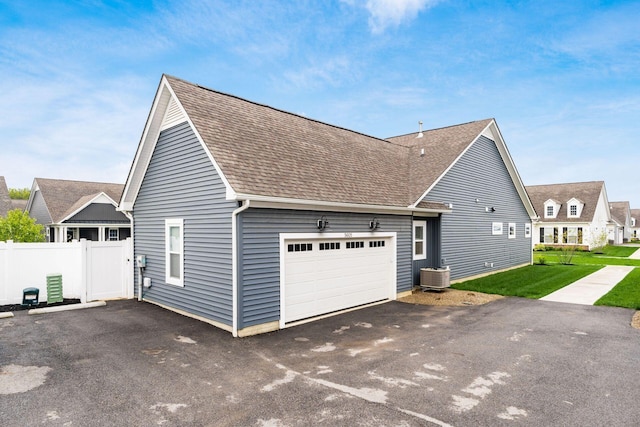 view of property exterior with fence, aphalt driveway, an attached garage, central AC unit, and roof with shingles