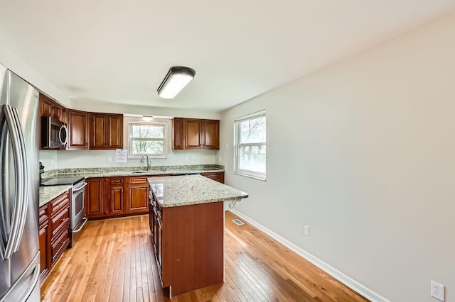 3861 Trestle Ct, Columbus, OH 43204 - kitchen with stainless steel appliances, a sink, light wood-style flooring, a center island, and light stone counters