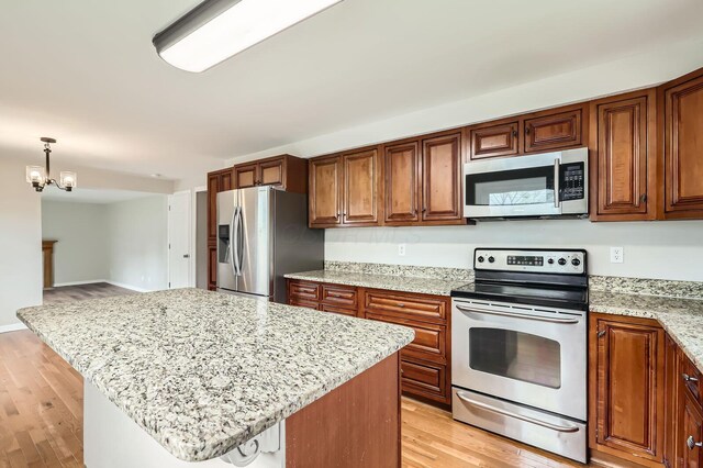 3861 Trestle Ct, Columbus, OH 43204 - kitchen with appliances with stainless steel finishes, light wood finished floors, brown cabinetry, and light stone countertops
