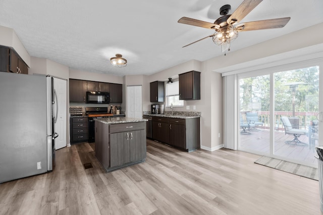 kitchen featuring dark brown cabinets, black microwave, stove, freestanding refrigerator, and light wood-type flooring