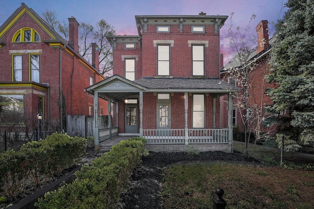 italianate-style house with covered porch, brick siding, and fence