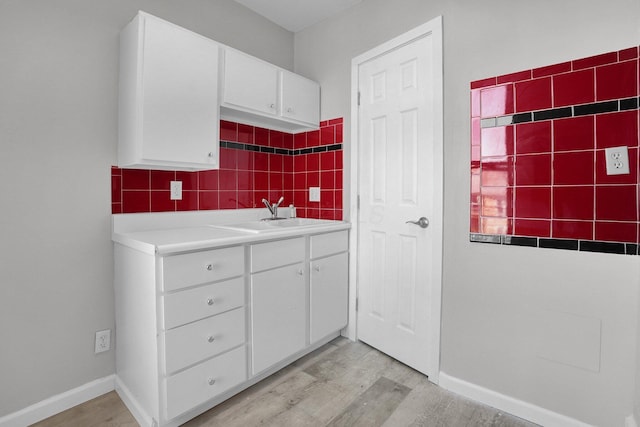 kitchen with white cabinets, a sink, light wood-style floors, light countertops, and backsplash