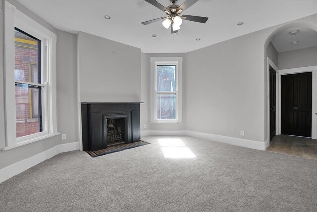 unfurnished living room with arched walkways, baseboards, a ceiling fan, and carpet