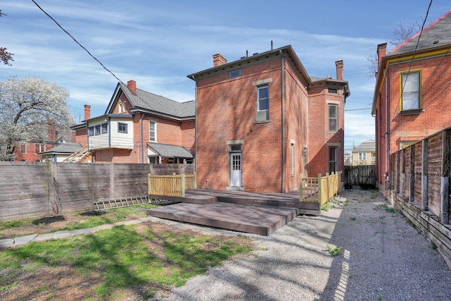 rear view of house with a fenced backyard, a wooden deck, a chimney, and brick siding