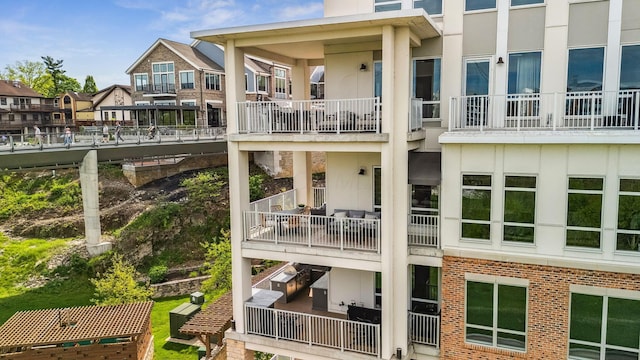 back of property with a balcony, brick siding, a residential view, and stucco siding