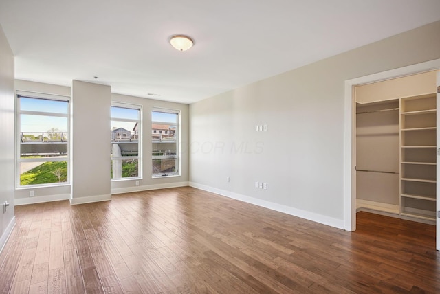 unfurnished bedroom featuring wood finished floors, a spacious closet, and baseboards