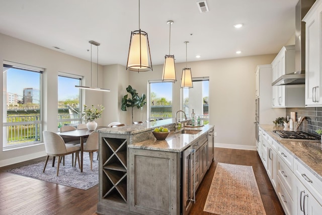 kitchen with a sink, an island with sink, baseboards, wall chimney range hood, and stainless steel appliances