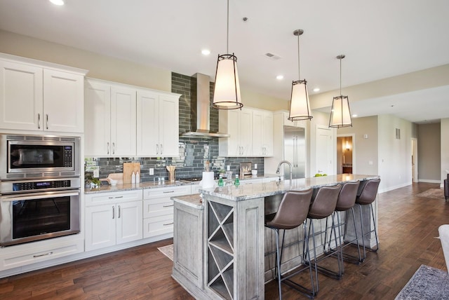 kitchen featuring built in appliances, wall chimney exhaust hood, tasteful backsplash, white cabinets, and recessed lighting