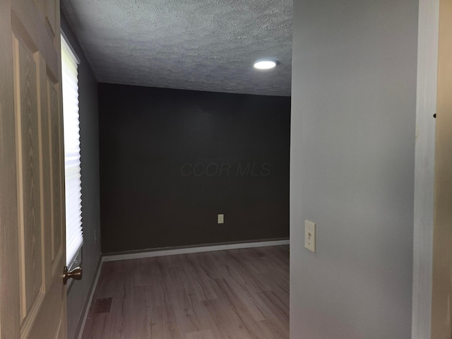 empty room with wood finished floors, baseboards, a textured ceiling, and visible vents