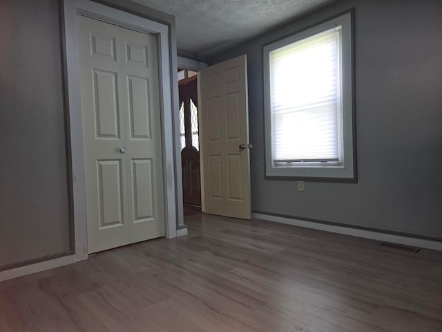 unfurnished bedroom with light wood finished floors, a textured ceiling, baseboards, a baseboard heating unit, and visible vents